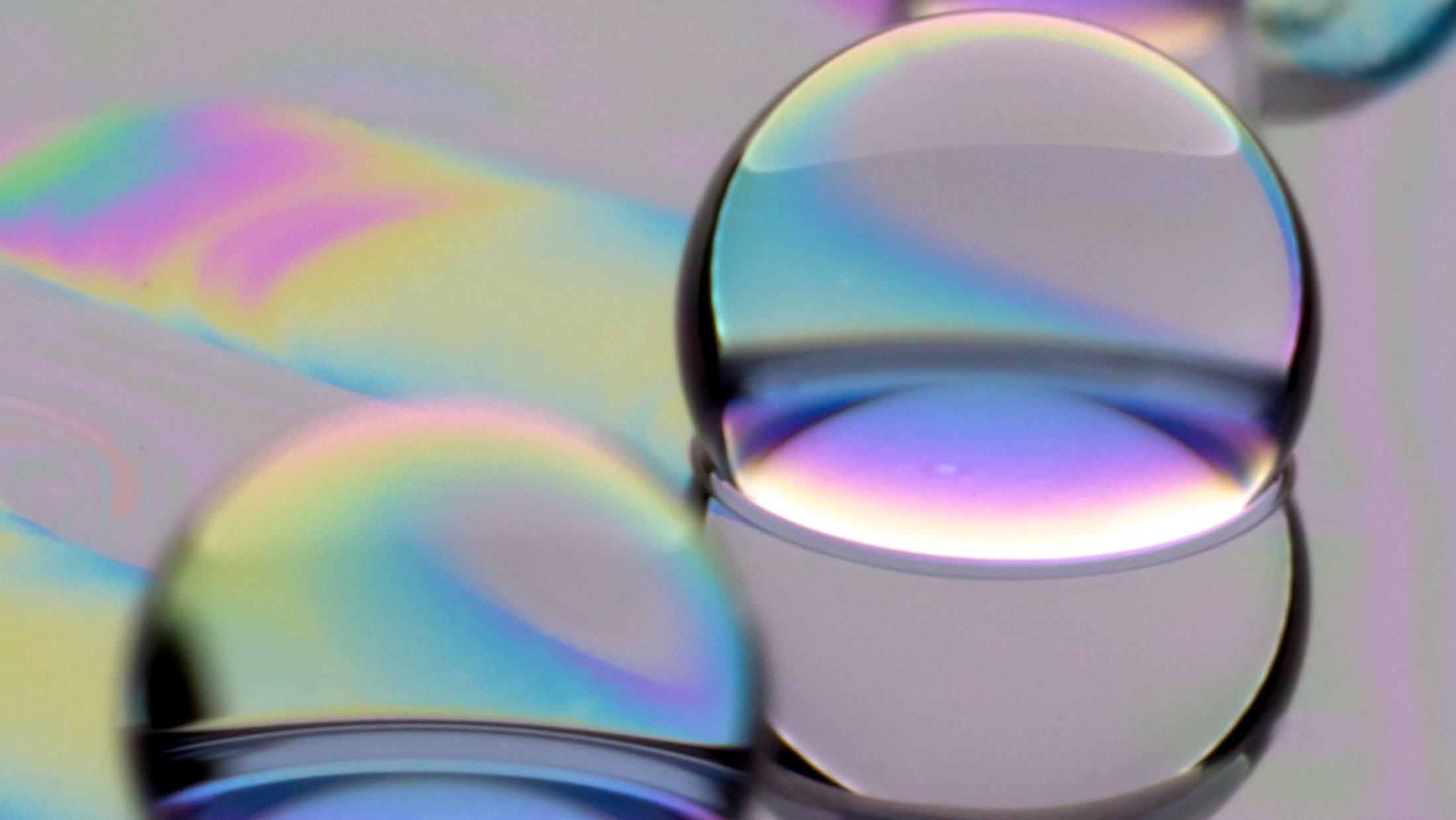 Iridescent oil droplets oleoplaning across a lubricated surface, showing thin-film interference.